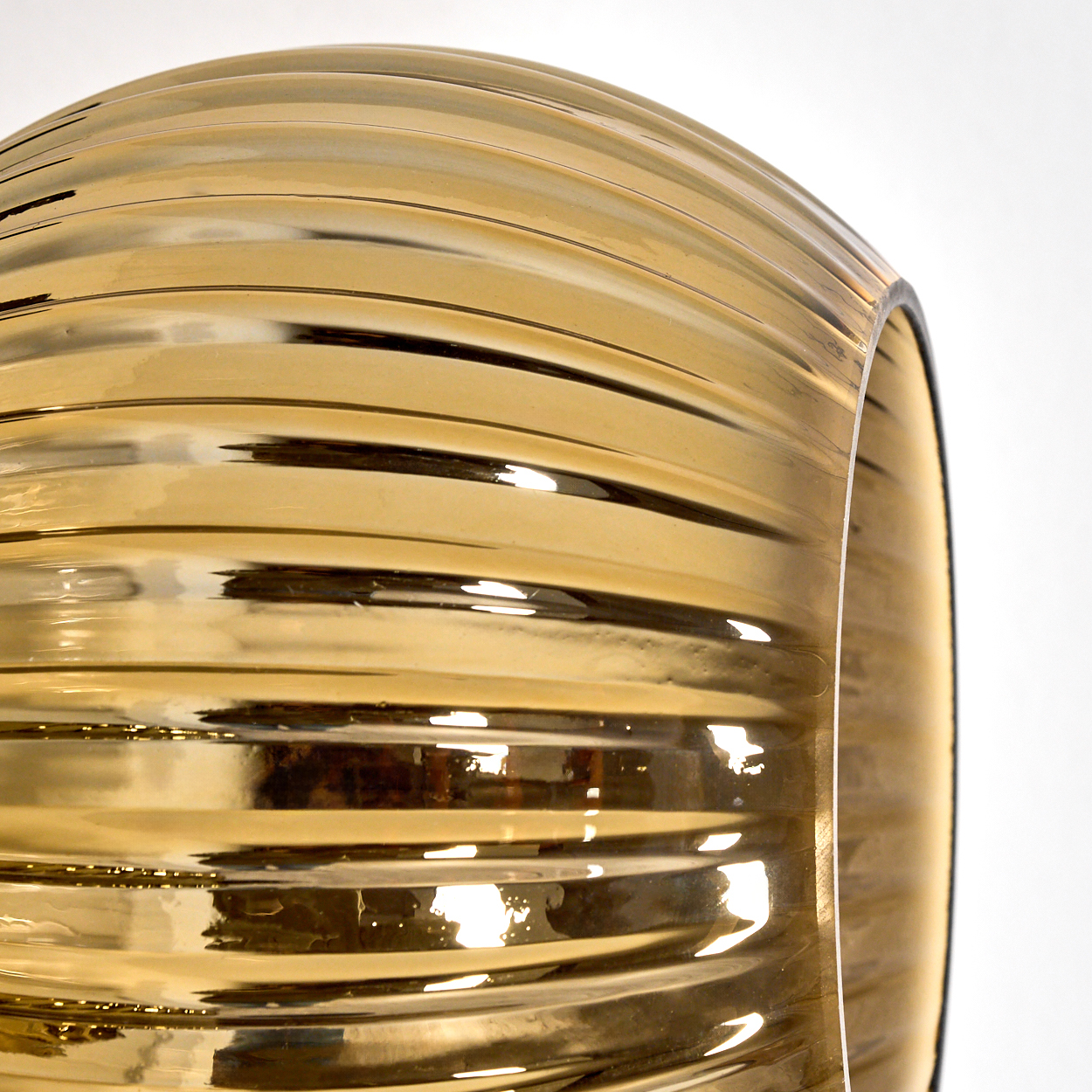 Nahaufnahme eines goldenen Glaslampenschirms mit gebogenen Rippen. Der Hintergrund ist weiß.