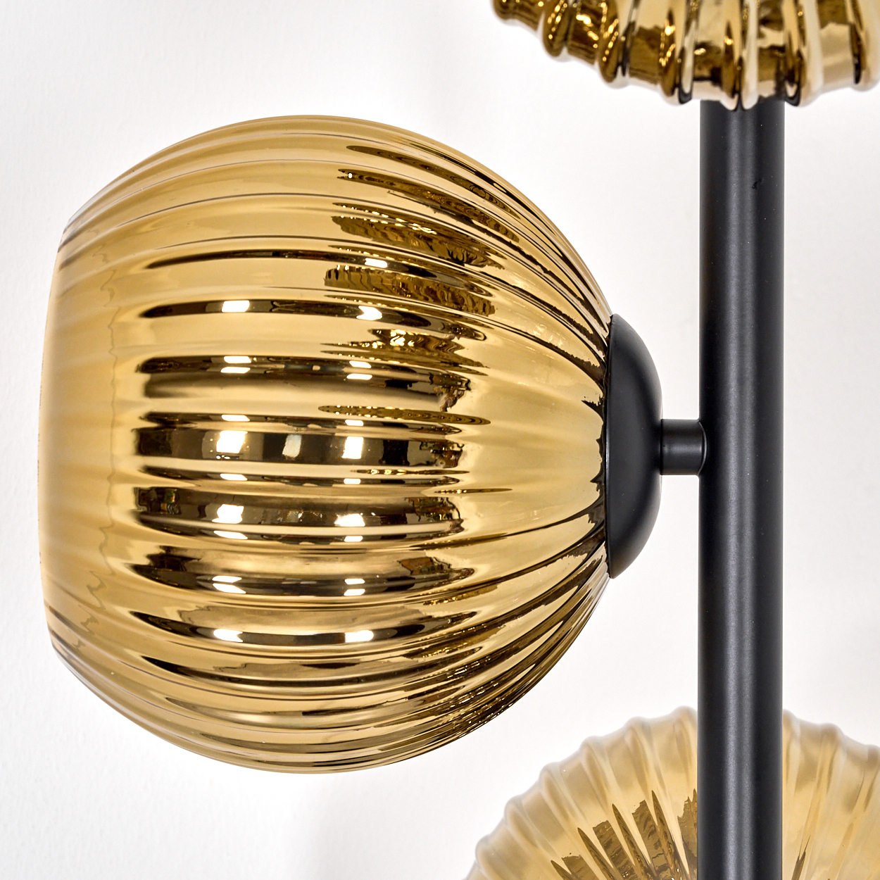 Nahaufnahme einer goldenen Lampe mit schwarzem Stiel. Die Lampe hat einen gerippten, ovalen Schirm und steht vor weißem Hintergrund.