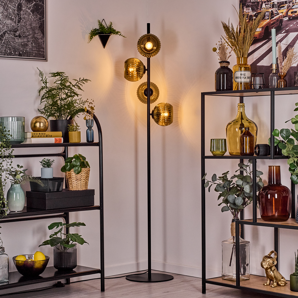 Ein Raum mit schwarzen Regalen, Pflanzen und einer Stehlampe mit bernsteinfarbenen Glasschirmen. Eine Karte und Dekor sind auf den Regalen.
