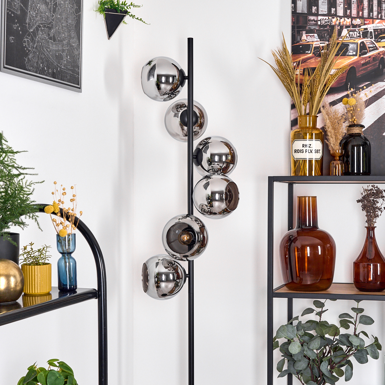 Eine moderne Stehlampe mit sechs reflektierenden Kugeln. Regale zeigen Vasen, Pflanzen und ein Foto von New York City.