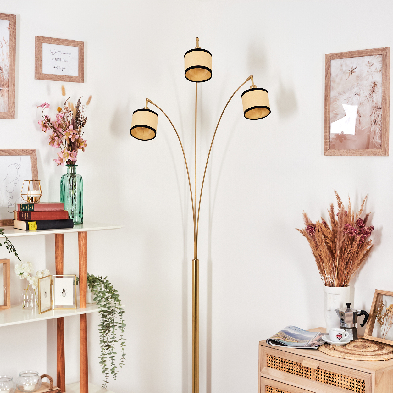 Ein Raum mit einer hohen Lampe, gerahmten Bildern und dekorativen Gegenständen. Ein Regal und ein Holzschrank sind ebenfalls sichtbar.