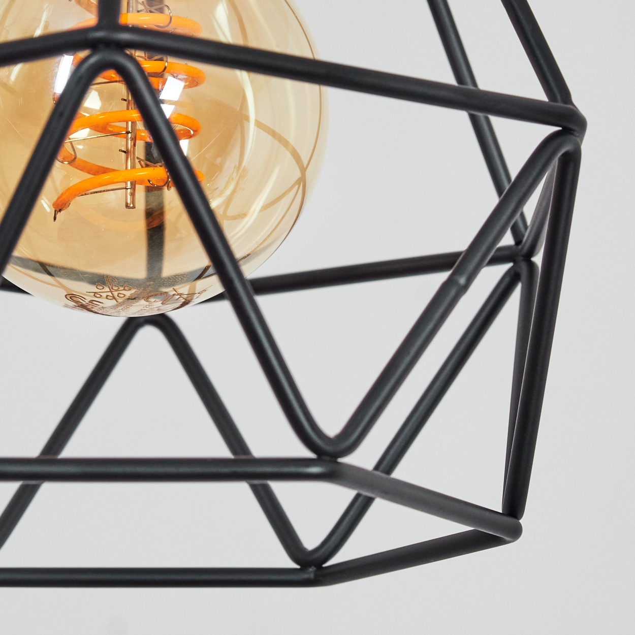 Nahaufnahme eines schwarzen, geometrischen Lampenschirms mit einer warm getönten Glühbirne. Der Hintergrund ist weiß.