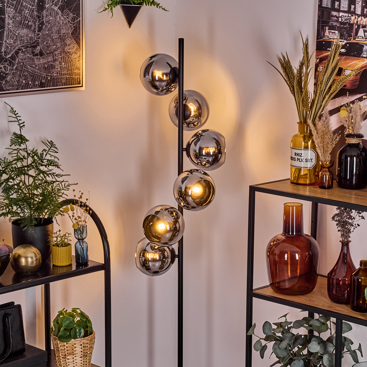 Ein modernes Wohnzimmer mit einer schwarzen Stehlampe mit Glaskugeln. Regale mit Vasen und Pflanzen. Eine Karte und ein Bild an der Wand.