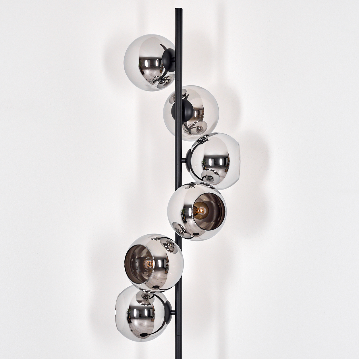 Eine moderne Lampe mit sechs verchromten Kugeln steht vor einer weißen Wand. Die Kugeln reflektieren den Raum. Ein schwarzer Pfahl stützt die Kugeln.