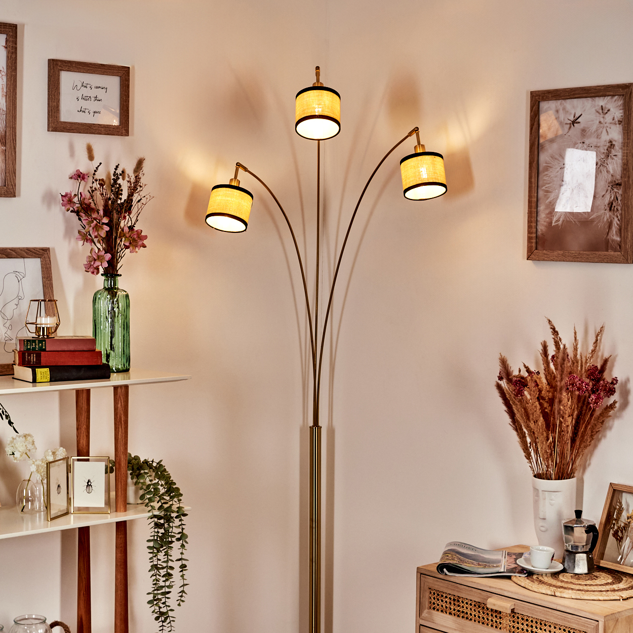 Ein Raum mit Stehlampe und drei Lampenschirmen. Regale mit Vasen und Rahmen. Ein Holzschrank mit Kaffeeservice.