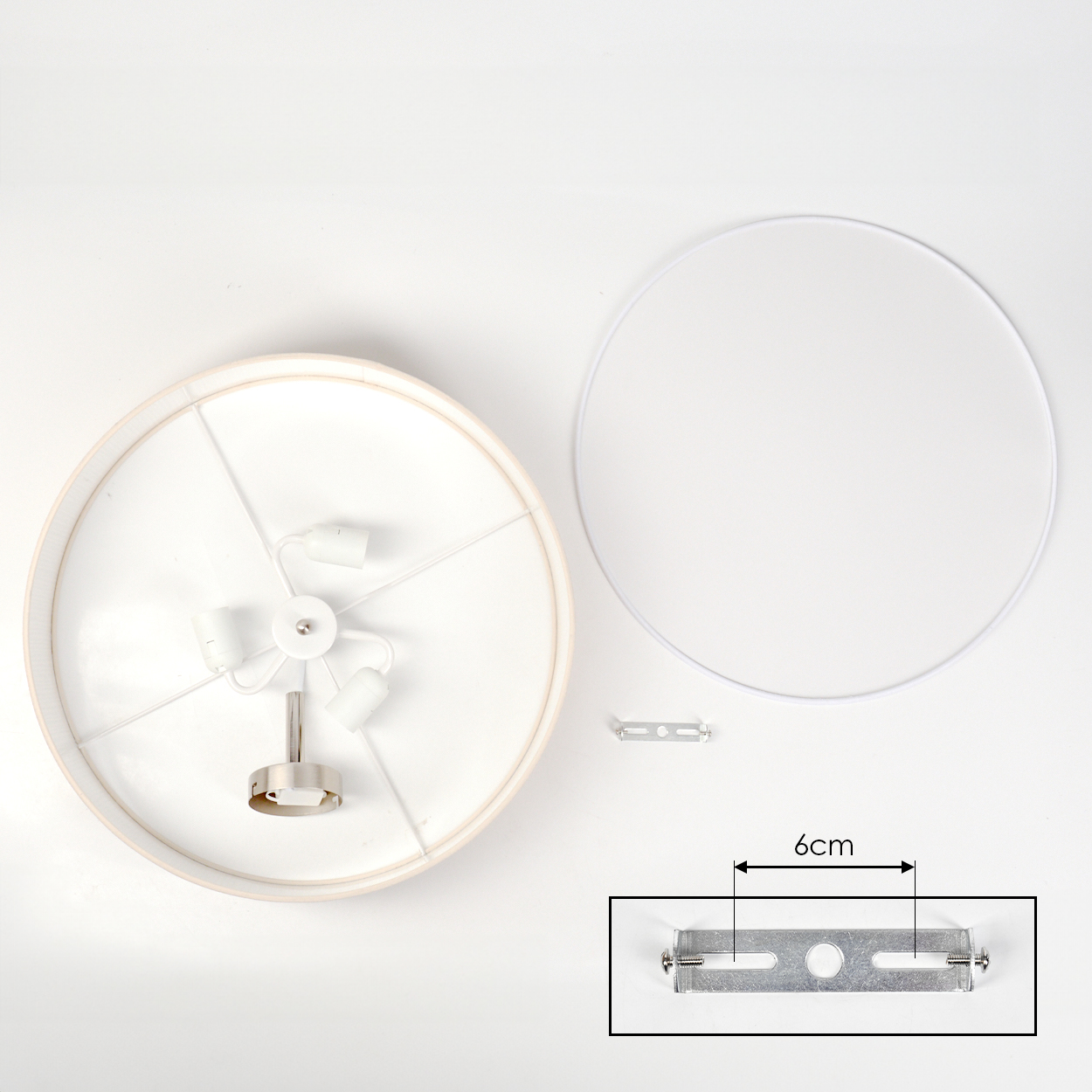 Eine zerlegte Lampe. Zu den Komponenten gehören ein Lampenschirm, ein Metallring, eine Halterung und ein Lampenhalter mit drei Fassungen.