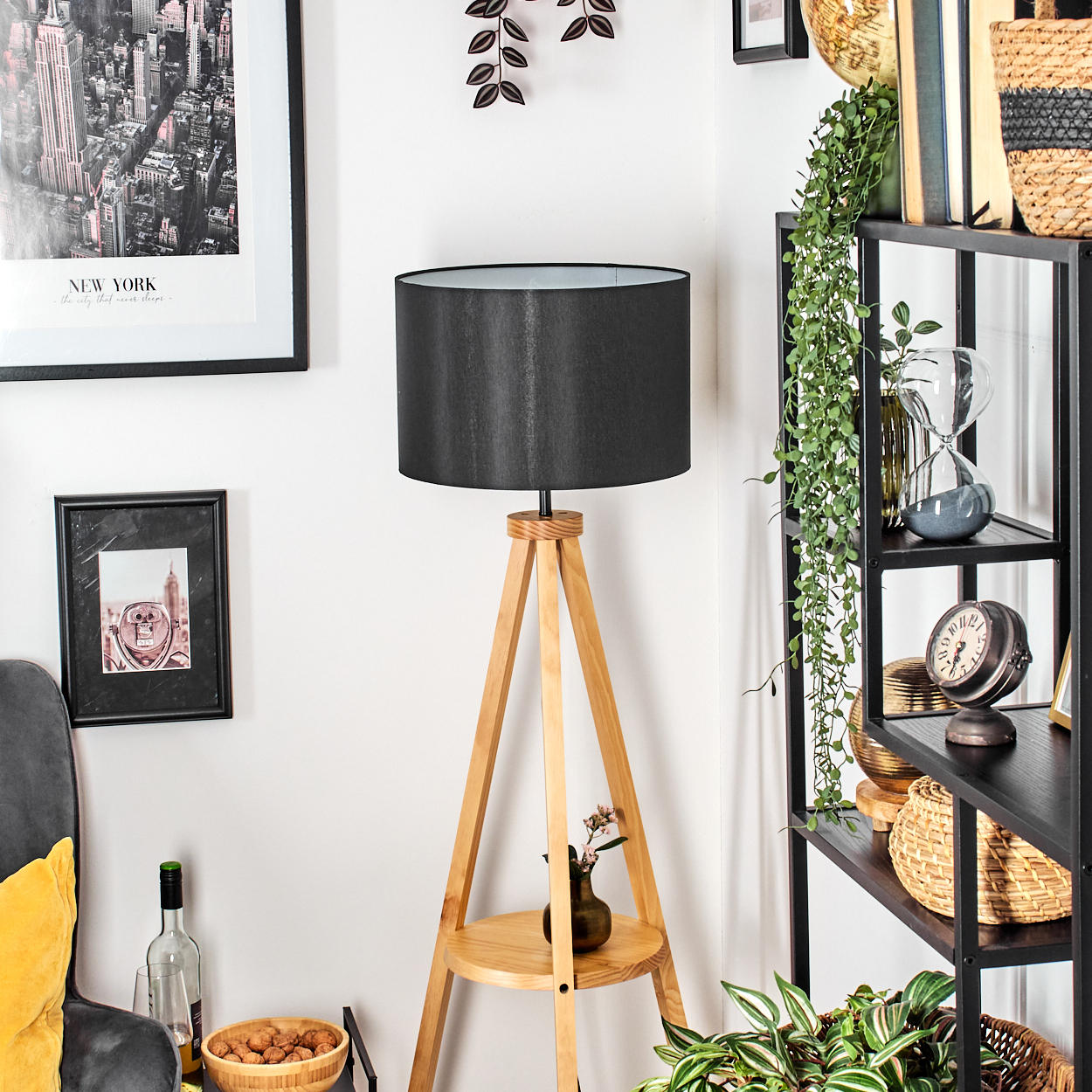 Ein Raum mit einer Holzlampe, einem schwarzen Lampenschirm, einem Regal mit Dekorationen und gerahmten Bildern an der Wand.
