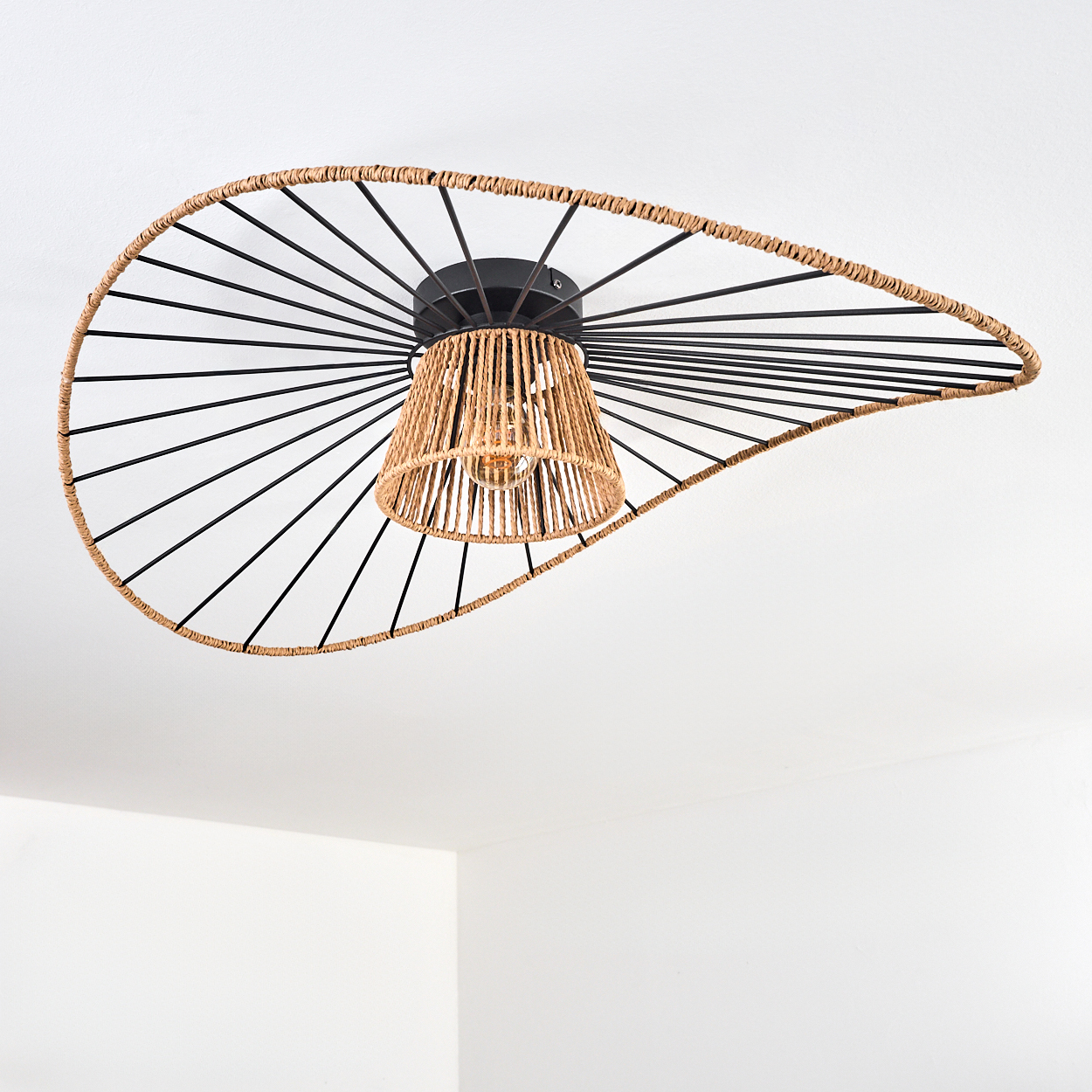 Dekorative Deckenlampe. Sie hat einen gewebten Lampenschirm und einen schwarzen Metallrahmen. Der Hintergrund ist eine weiße Decke.