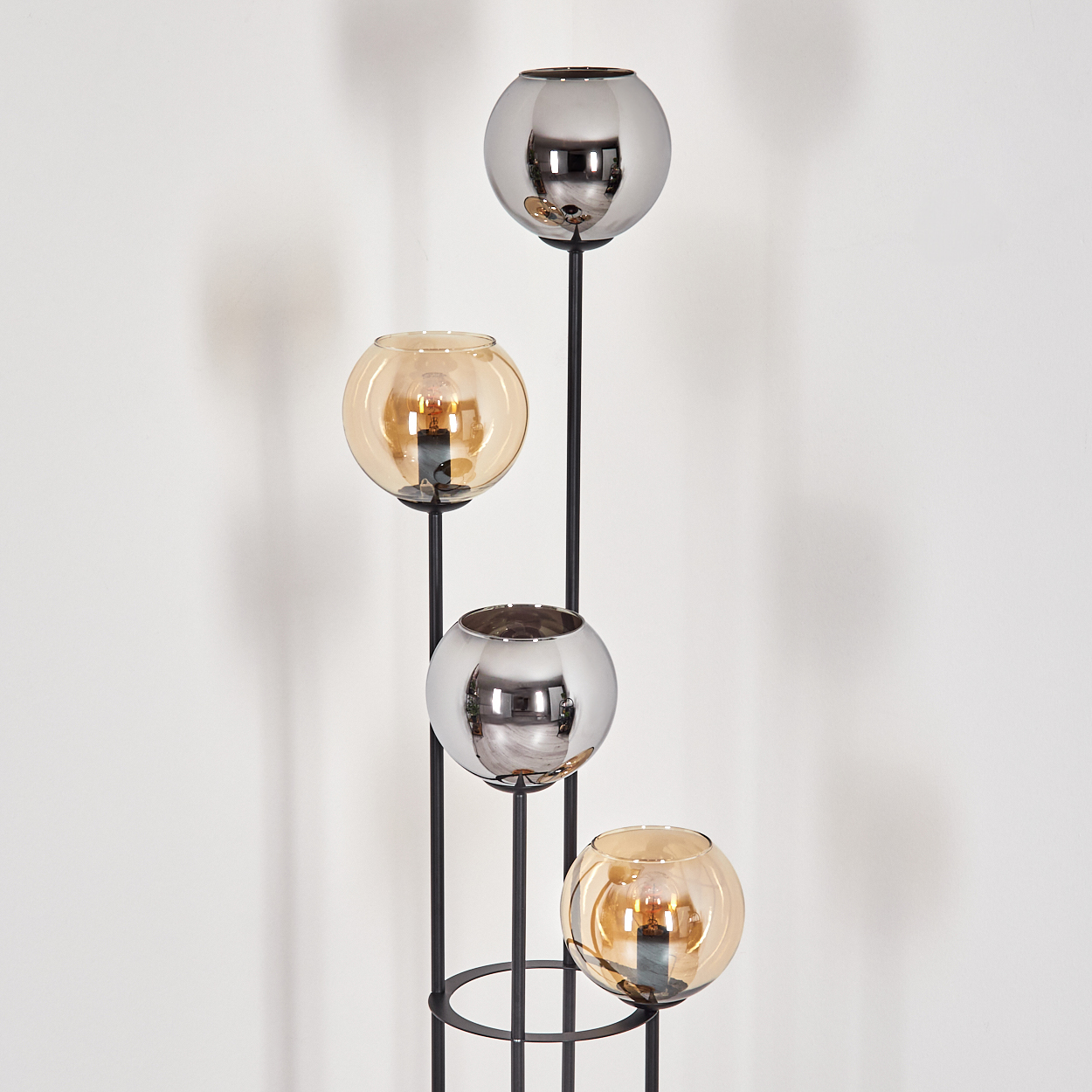 Eine moderne Stehlampe mit vier kugelförmigen Lichtern. Die Kugeln wechseln sich zwischen silbernem und bernsteinfarbenem Glas ab, auf einem schwarzen Metallrahmen.