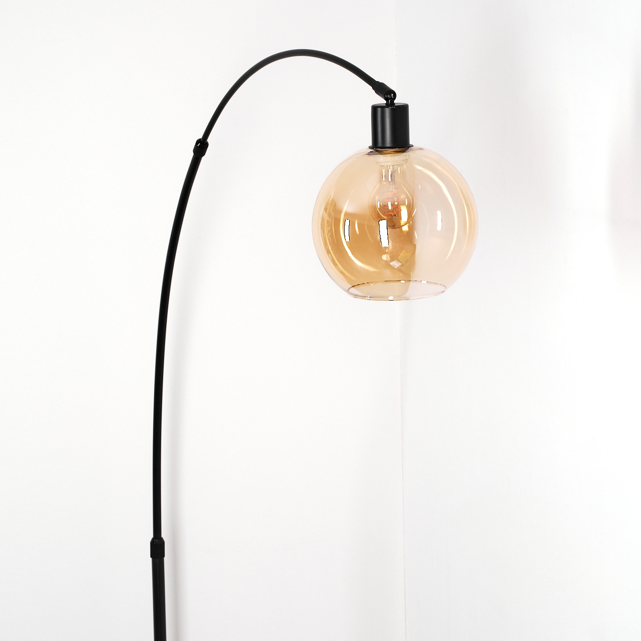 Eine moderne schwarze Stehlampe mit einem kugelförmigen, bernsteinfarbenen Glasschirm. Die Lampe steht in einer Ecke mit weißen Wänden.