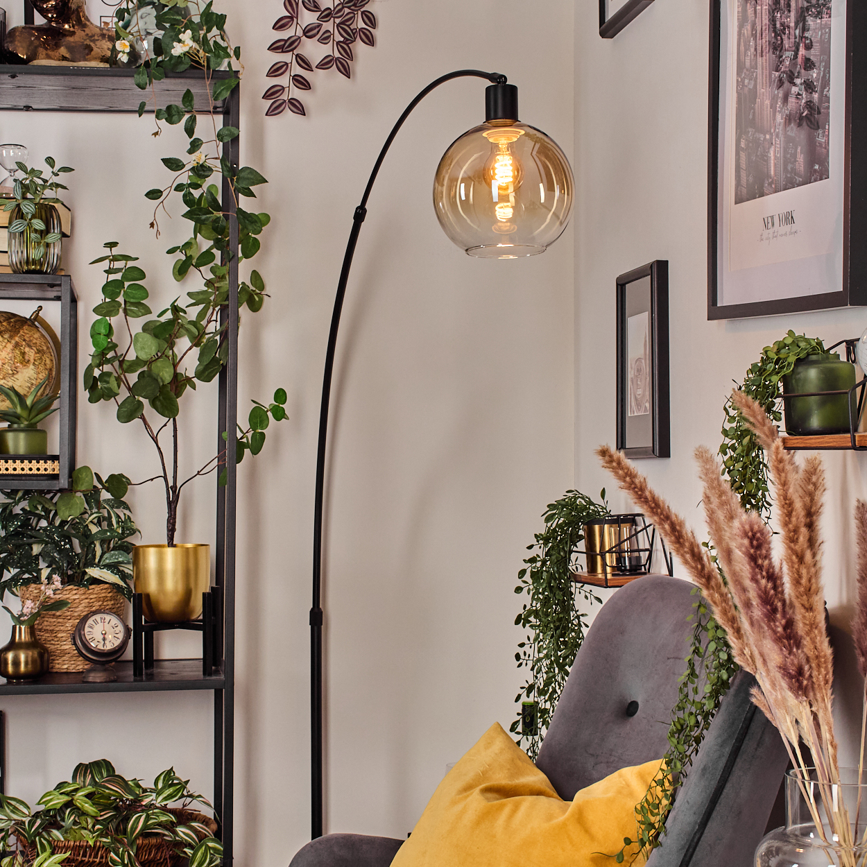 Ein Raum mit einer schwarzen Stehlampe, Pflanzen, einem grauen Stuhl mit gelbem Kissen und einem New York-Bild an der Wand.