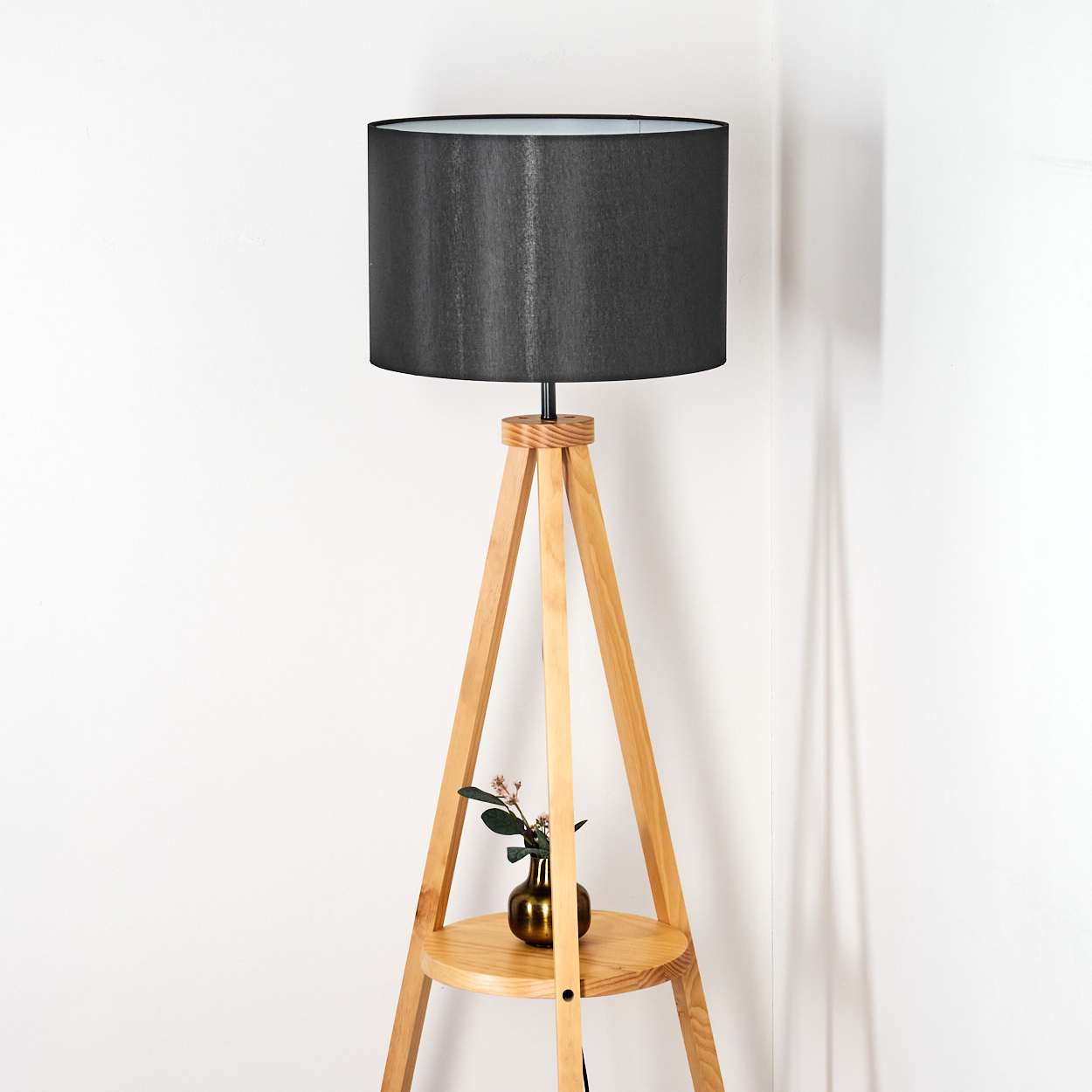 Eine moderne Stehlampe aus Holz mit schwarzem Lampenschirm. Eine kleine Vase mit Blumen steht auf einem Regal.