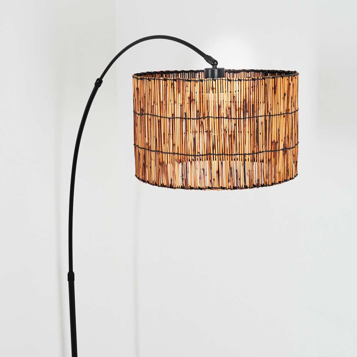 Eine moderne Stehlampe mit Bambus-Lampenschirm und schwarzem Metallrahmen. Sie steht vor einer weißen Wand.
