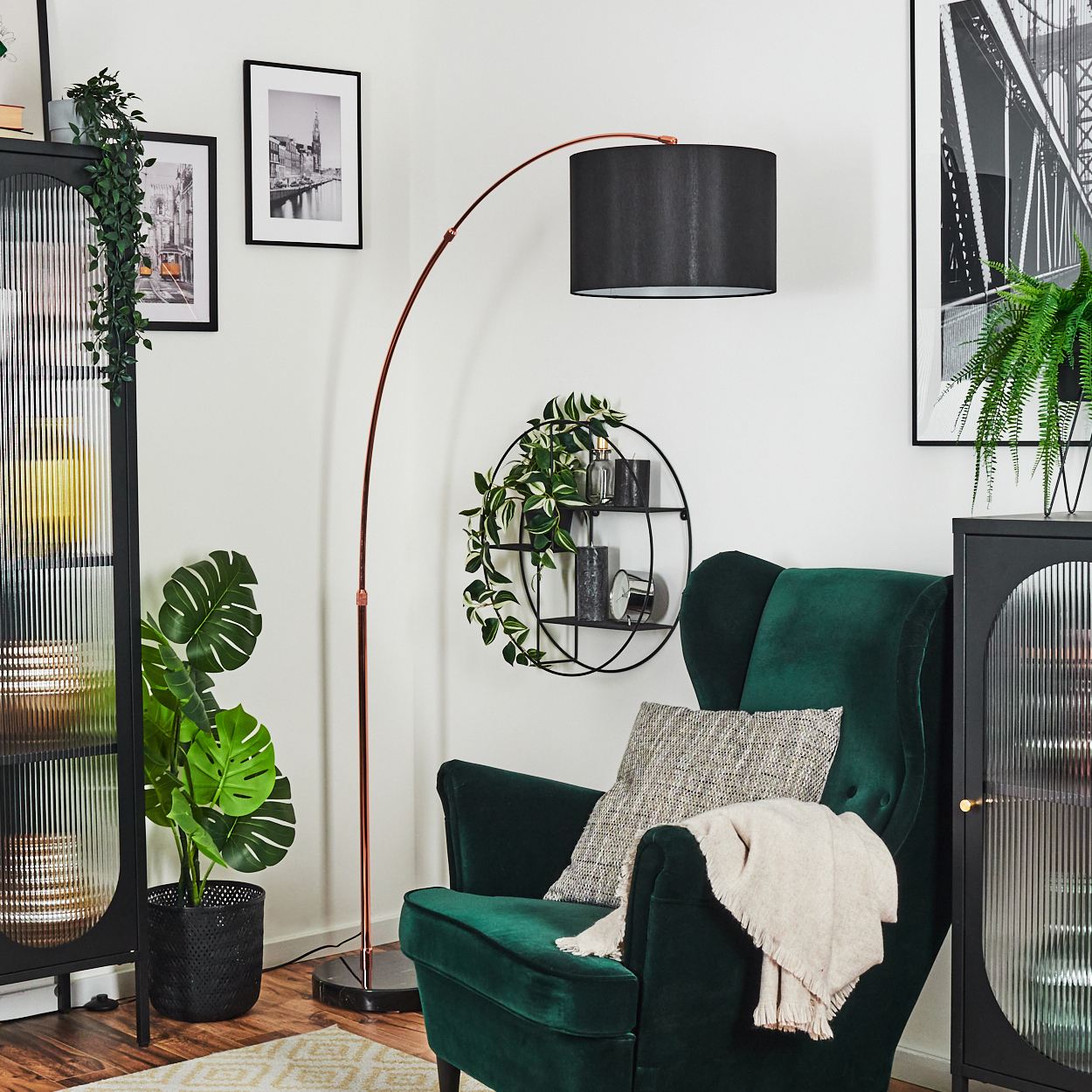 Ein grüner Sessel mit Decke und Kissen, eine kupferfarbene Stehlampe, schwarze Schränke und Wandkunst mit Pflanzen.