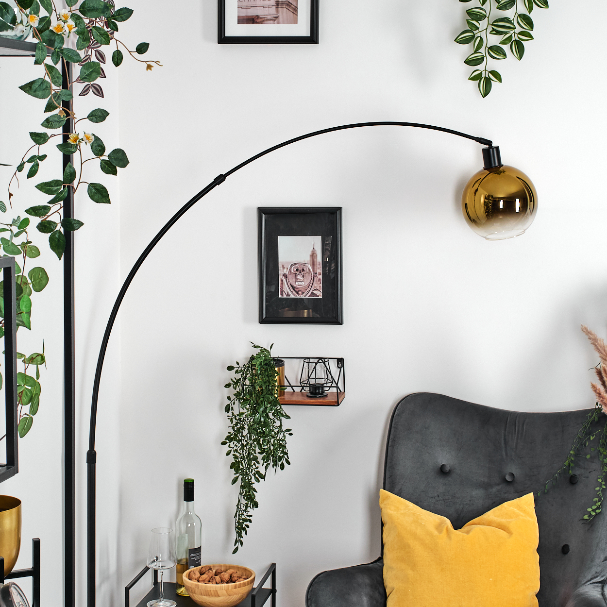 Ein Raum mit Stehlampe, Kunst, grauem Stuhl mit gelbem Kissen und Pflanzen. Ein Tisch hat Wein und eine Schüssel Nüsse.