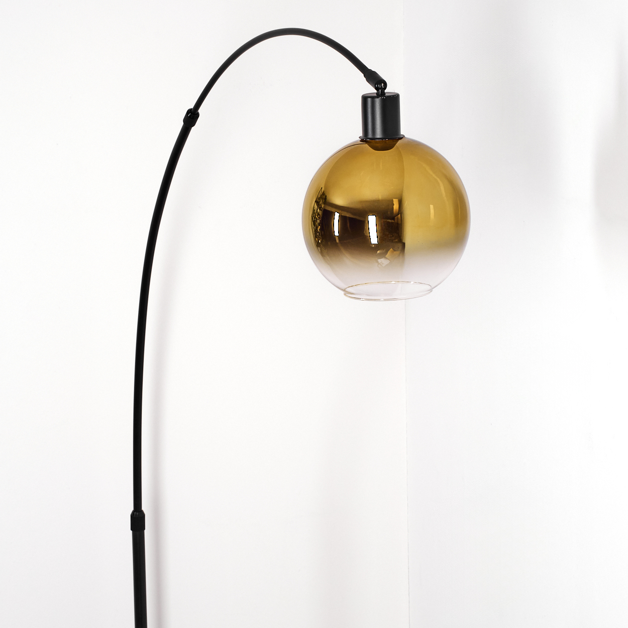 Eine moderne Stehlampe mit einem schwarzen gebogenen Arm und einem kugelförmigen, bernsteinfarbenen Glasschirm. Der Hintergrund ist eine weiße Wand.