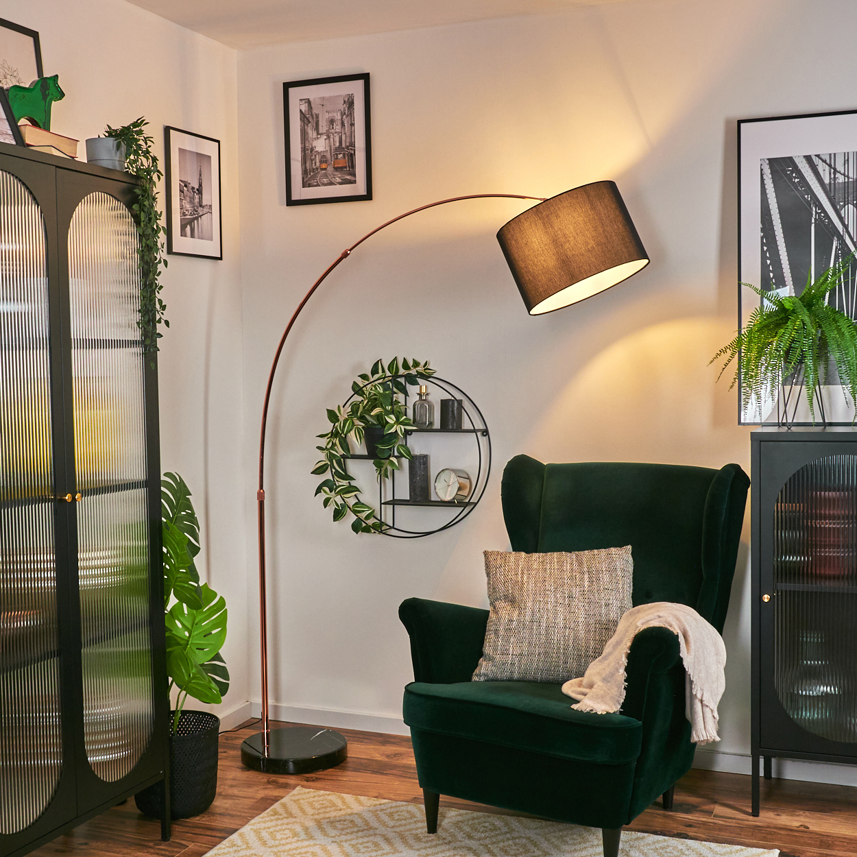 Ein dunkelgrüner Sessel mit Decke und Kissen, eine schwarze Lampe, ein schwarzer Schrank mit Pflanzen und ein kleiner Teppich.