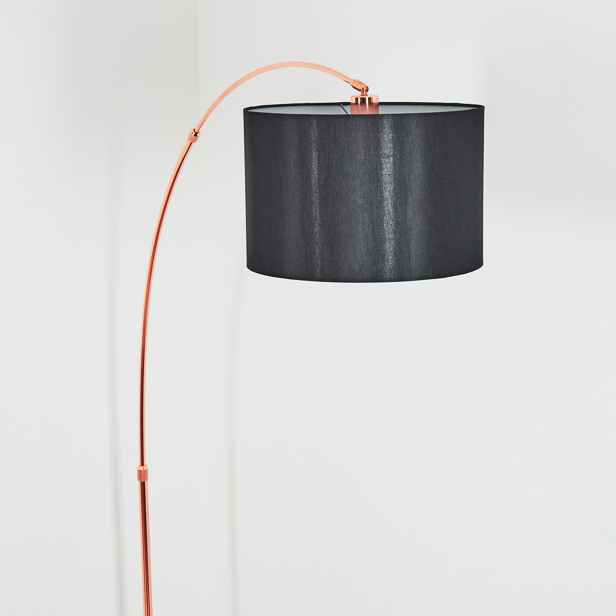 Eine moderne Stehlampe mit gebogenem kupferfarbenem Rahmen und schwarzem Lampenschirm vor weißer Wand.