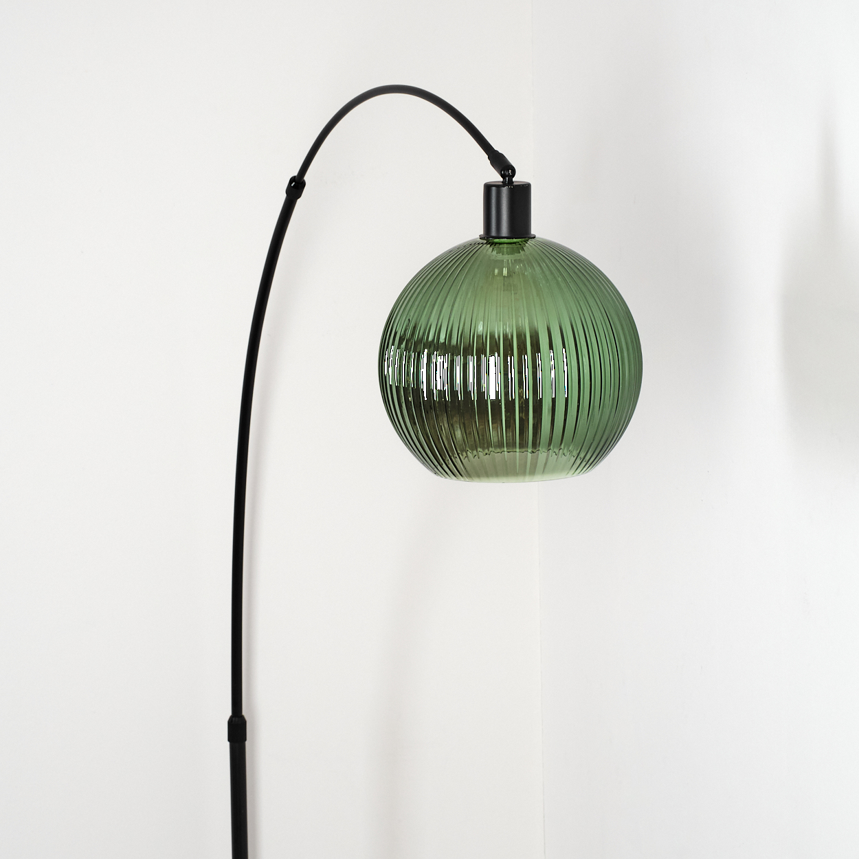 Eine moderne Lampe mit grünem Glasschirm und schwarzem Rahmen. Die Lampe steht vor einer weißen Wand.