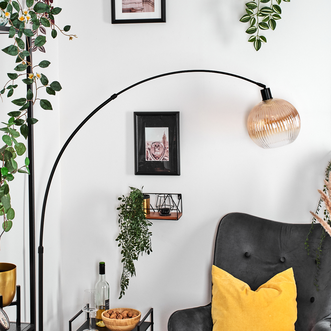 Ein modernes Wohnzimmer mit schwarzer Bogenlampe, grauem Sessel, gelbem Kissen und einem kleinen Tisch mit Snacks und Getränken.