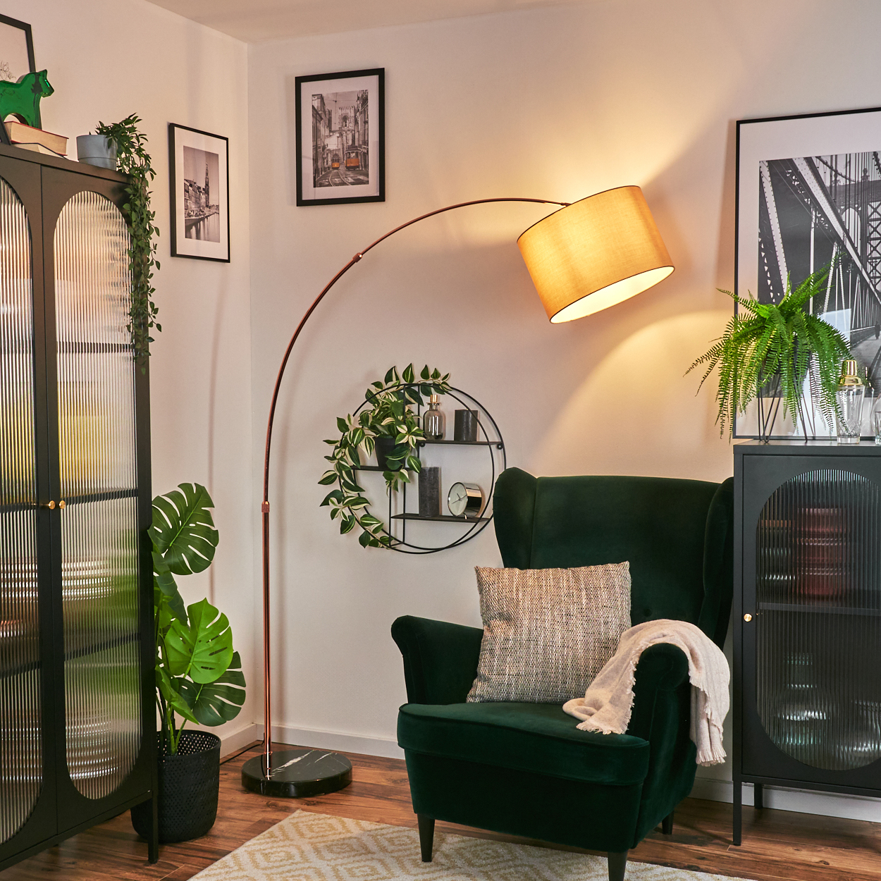 Ein dunkelgrüner Sessel mit Decke und Kissen. Eine Bogenlampe ragt darüber. Schwarze Schränke, Kunst und Pflanzen im Hintergrund.