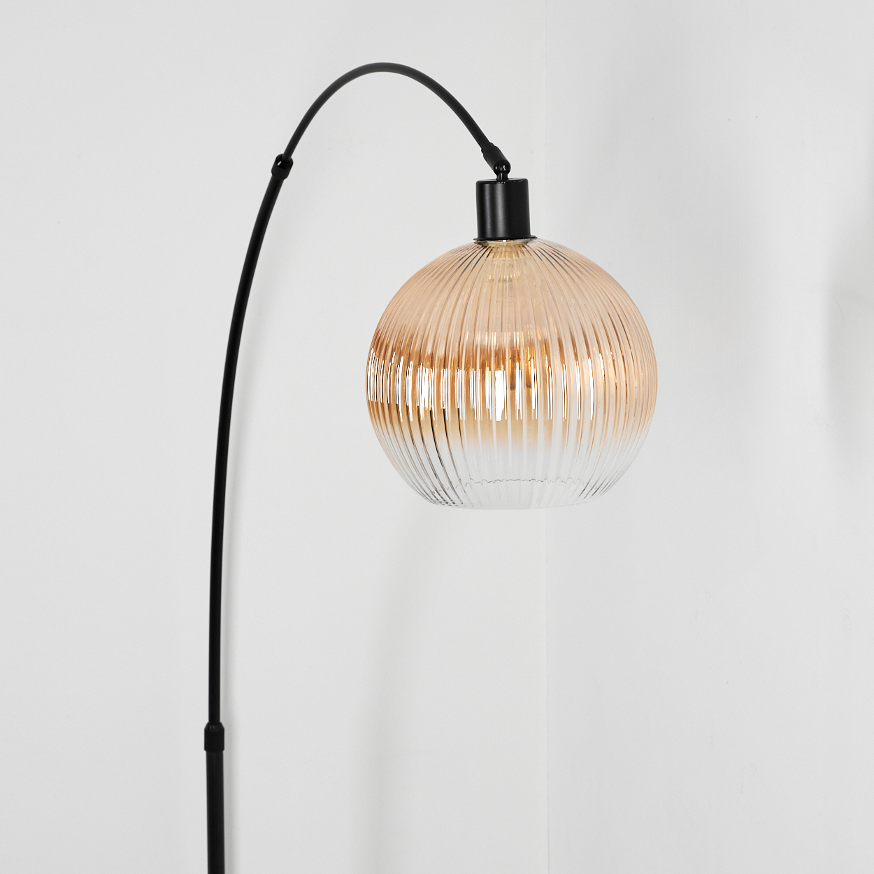 Eine moderne Stehlampe mit einem schwarzen, gebogenen Arm und einem runden, geriffelten Glasschirm in Bernstein und Weiß. Der Hintergrund ist weiß.