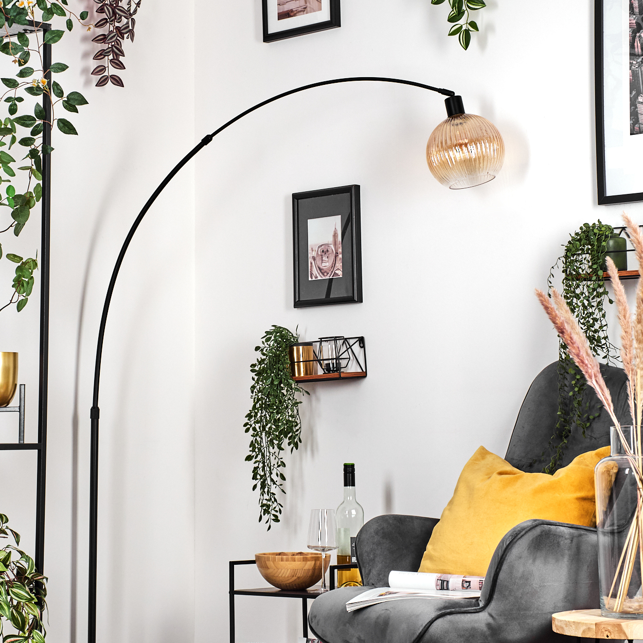 Ein modernes Wohnzimmer mit schwarzer Bogenlampe, grauem Sessel, gelbem Kissen und Zierpflanzen. Rechts eine Glasvase.