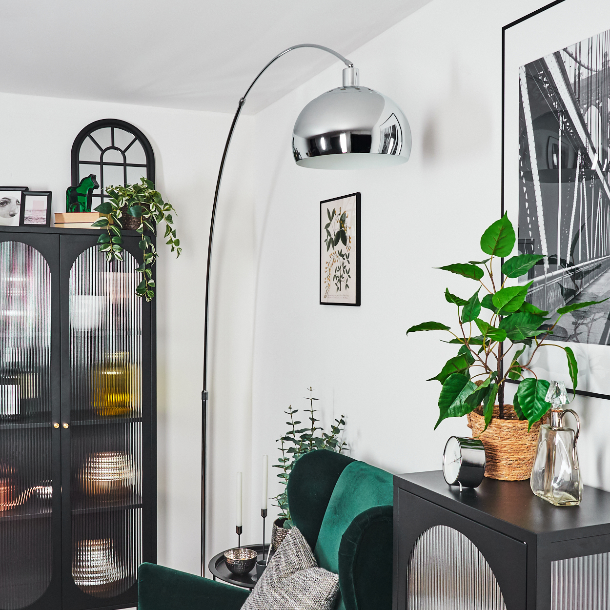 Wohnzimmer: schwarzer Schrank, grünes Sofa, Bogenlampe, Pflanze, Bilder. Silberne Bogenlampe, schwarze gerahmte Kunst und eine Pflanze.