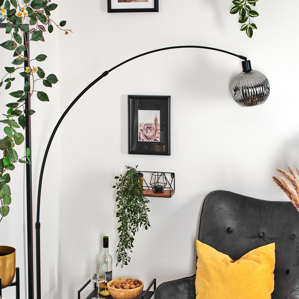 Ein modernes Wohnzimmer mit einer schwarzen Bogenlampe, einem grauen Stuhl mit gelbem Kissen und verschiedenen Dekorationselementen.