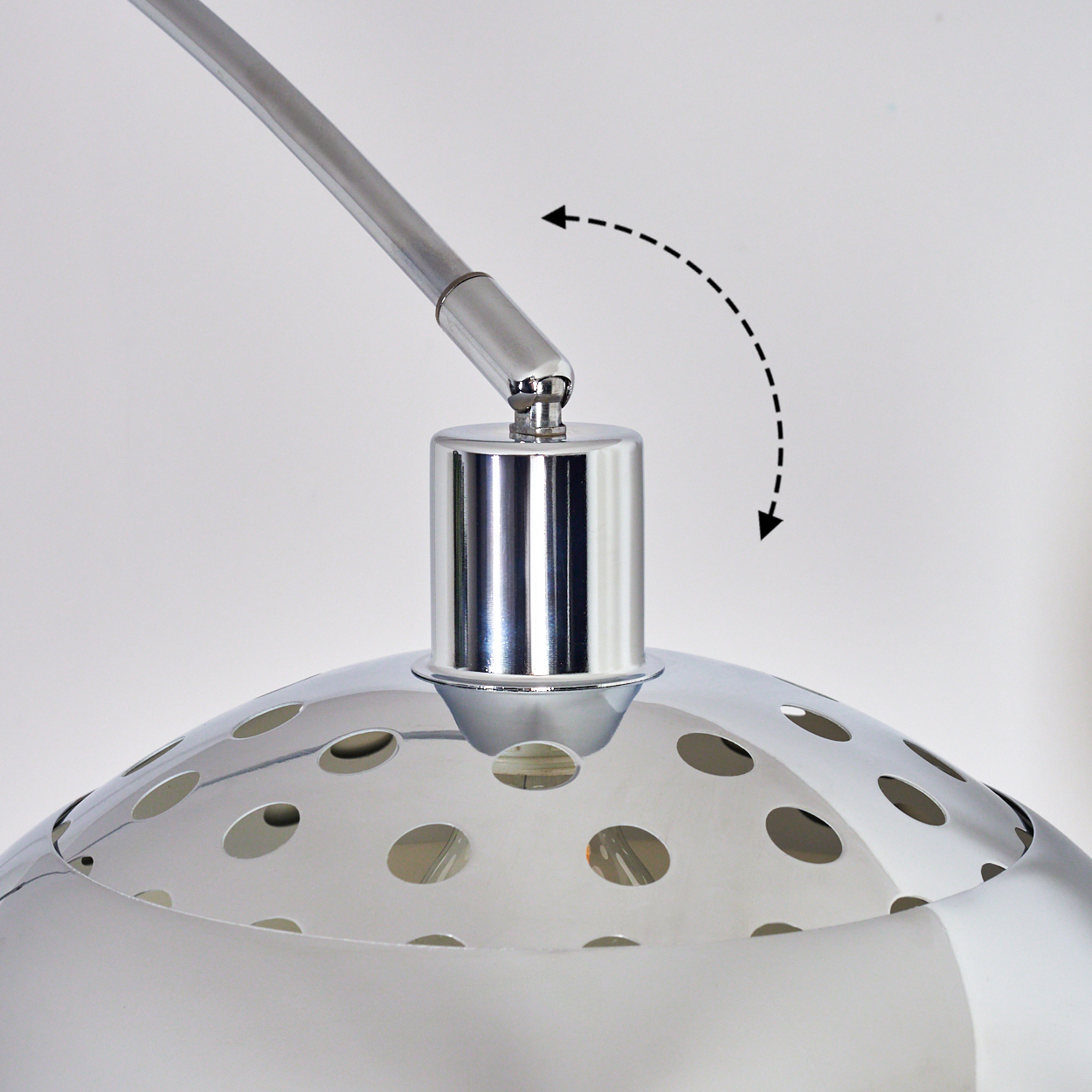 Eine Chromlampe mit gebogenem Arm. Der Lampenkopf hat kreisförmige Aussparungen. Ein gestrichelter Pfeil zeigt die verstellbare Bewegung.