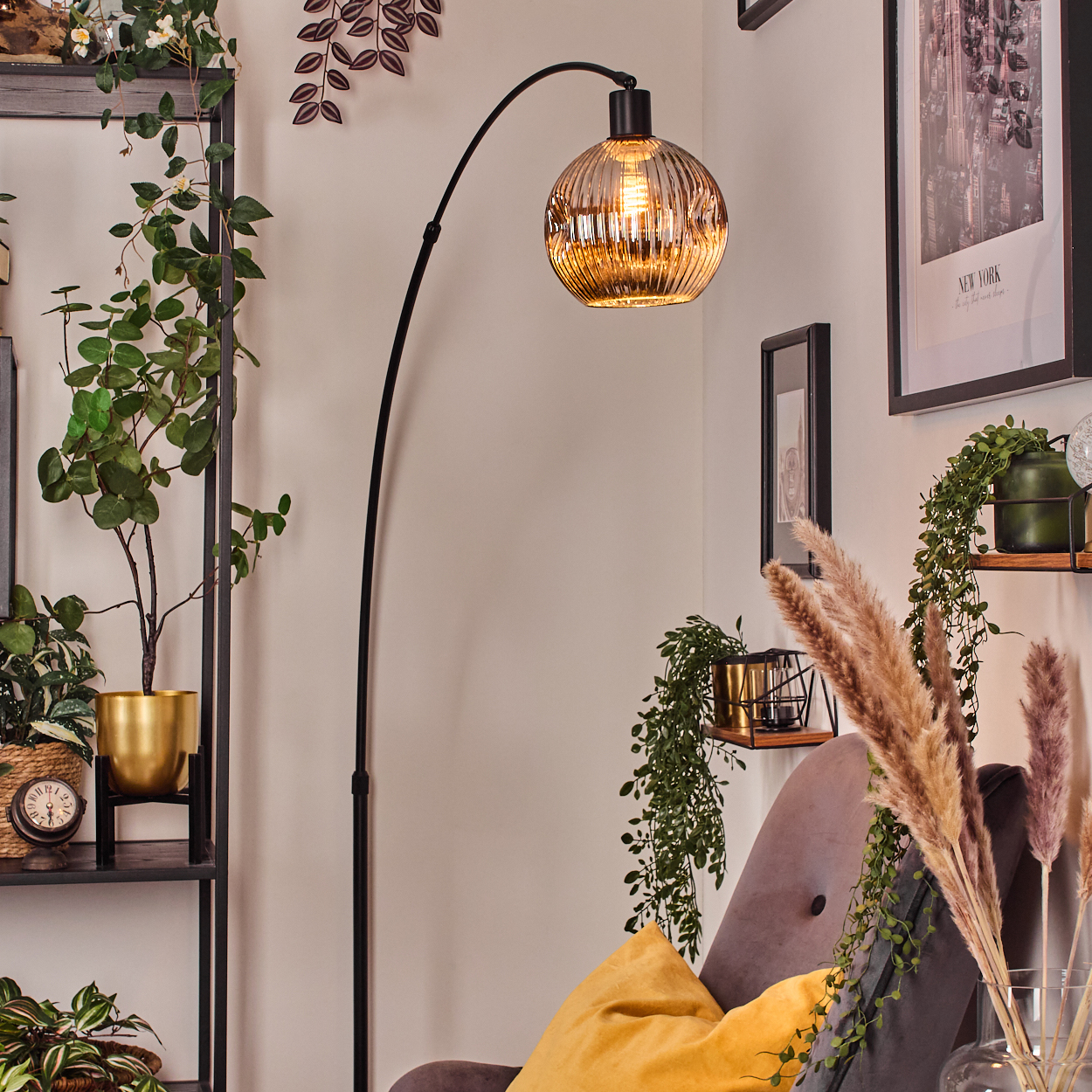 Ein Raum mit Pflanzen, einer Stehlampe, einem grauen Stuhl mit gelbem Kissen und gerahmten Bildern an der Wand.