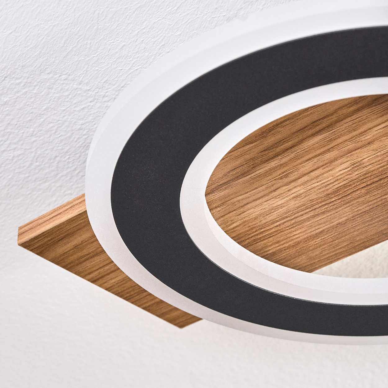 Eine moderne Deckenleuchte. Sie hat einen weißen Außenring, einen schwarzen Innenring und einen Holzsockel. Der Hintergrund ist eine weiße Decke.