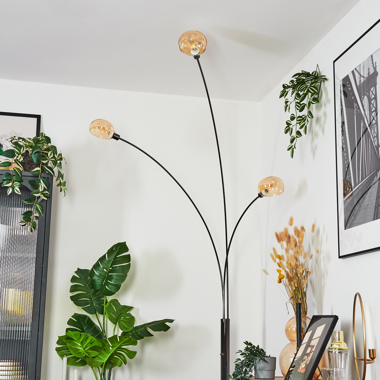 Eine moderne Stehlampe mit drei kugelförmigen Leuchten. Pflanzen und gerahmte Kunst im Hintergrund. Die Lampe ist schwarz.
