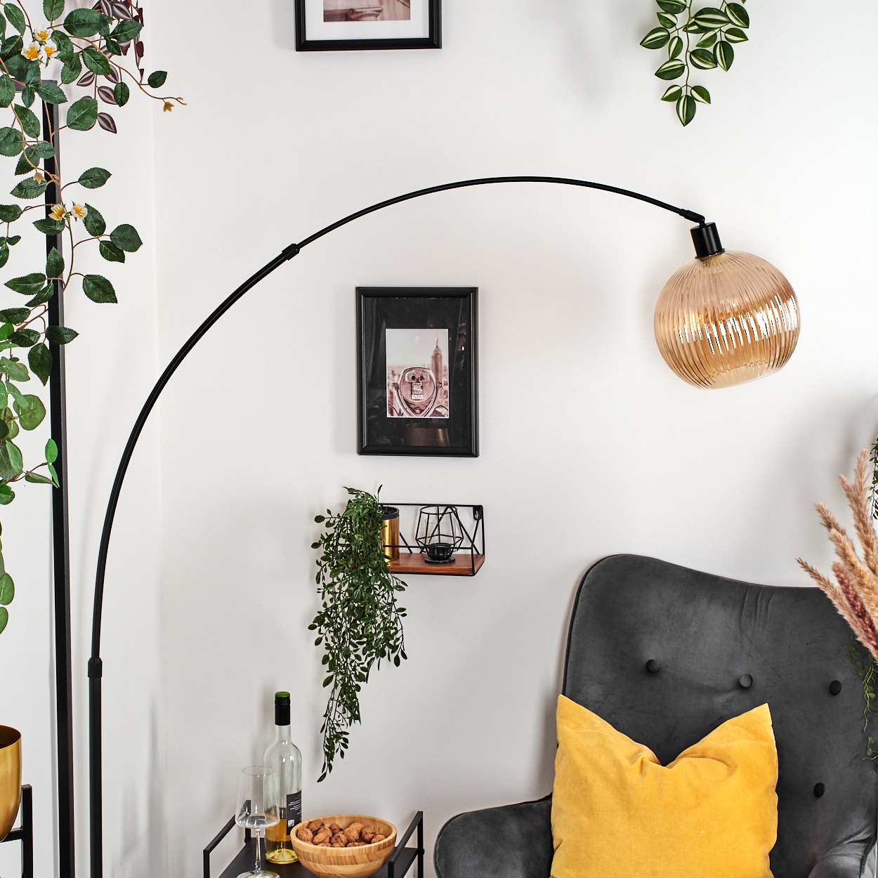 Ein modernes Interieur mit schwarzer Lampe, grauem Sessel mit gelbem Kissen und einer Wand mit Dekoration.