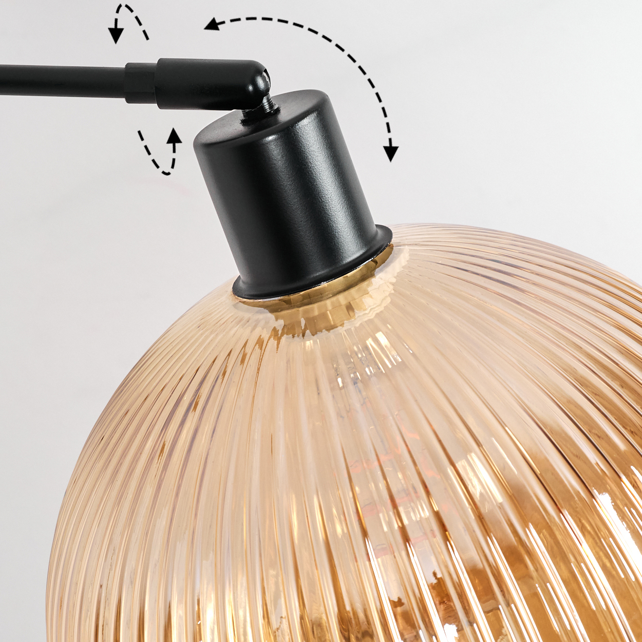 Nahaufnahme einer Lampe. Der Lampenschirm ist aus bernsteinfarbenem Glas mit vertikalen Linien. Der Lampenarm und das Gelenk sind schwarz.