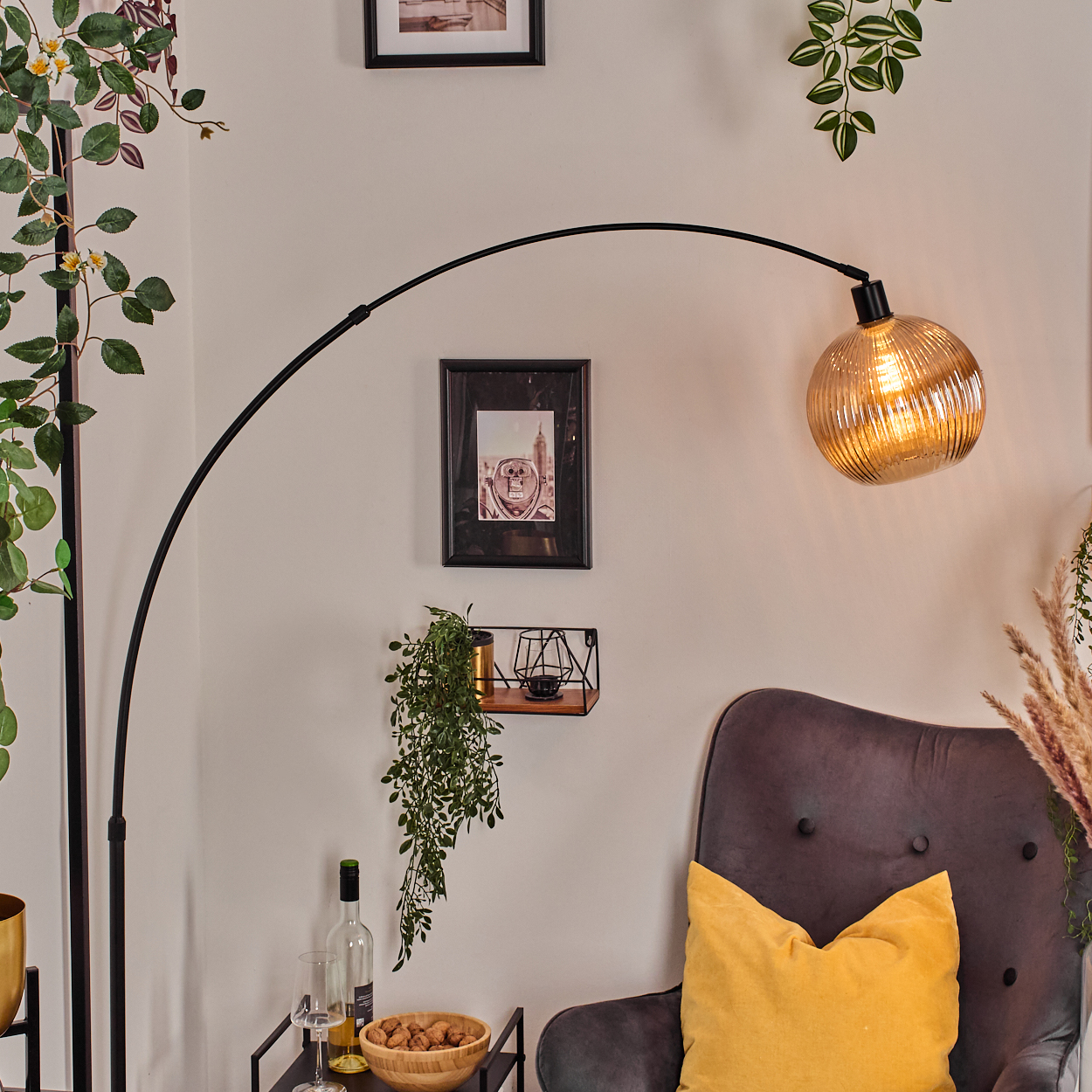 Ein modernes Wohnzimmer mit einer schwarzen Bogenlampe, einem grauen Sessel mit gelbem Kissen und Zierpflanzen.