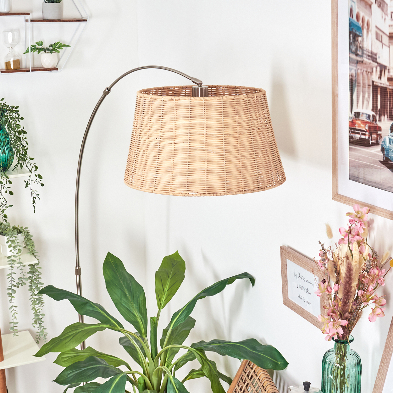 Ein gewebter Lampenschirm hängt über einer Pflanze. Ein gerahmtes Bild und eine Vase mit Blumen sind an der Wand.