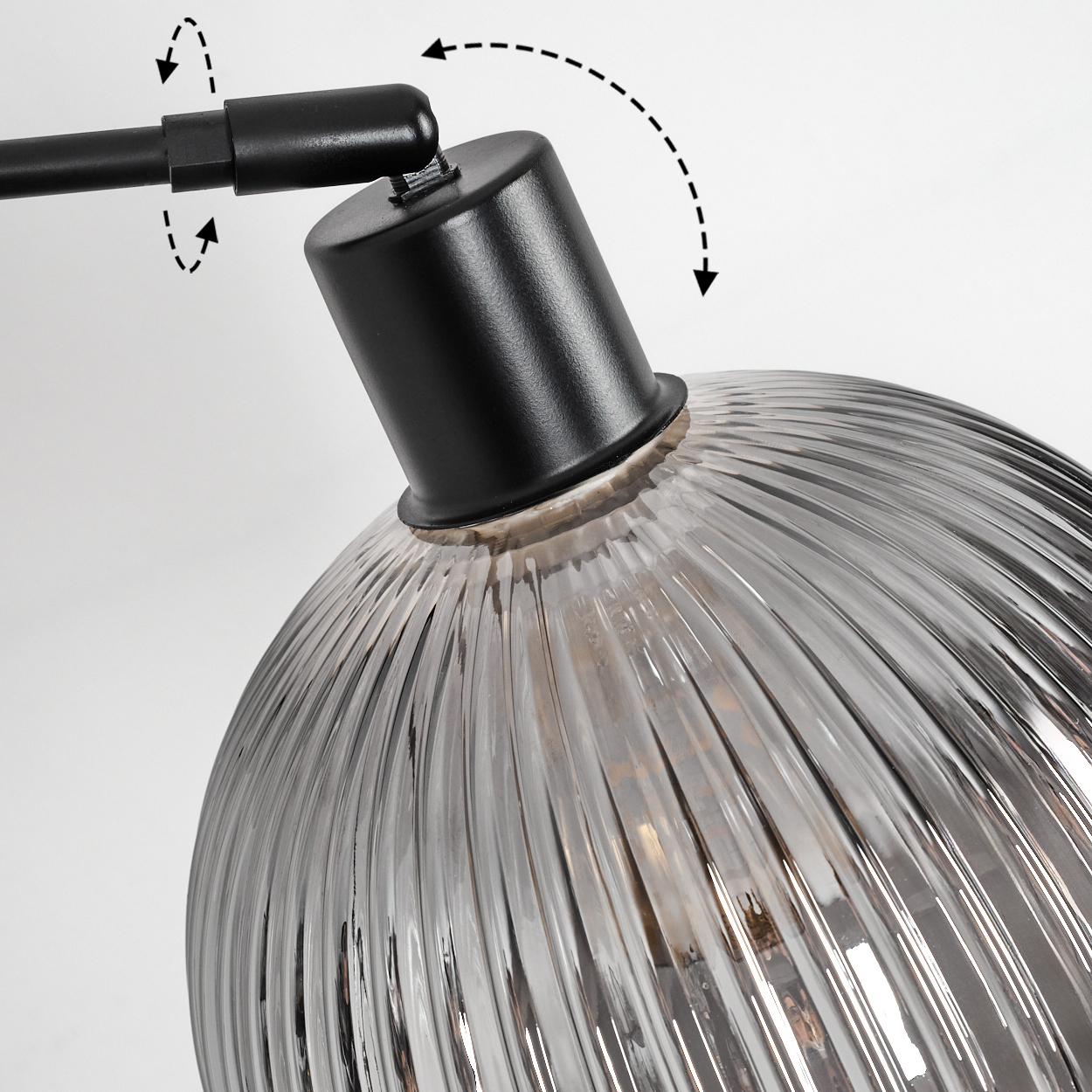 Nahaufnahme einer Lampe. Schwarzer, verstellbarer Arm, schwarzer zylindrischer Sockel und ein klarer, gerippter Glasschirm.