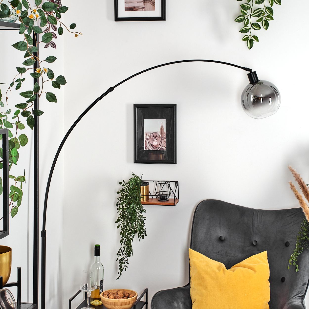 Ein Raum mit einer schwarzen Bogenlampe, einem grauen Sessel, einem gelben Kissen und einer Holzschale mit Nüssen.