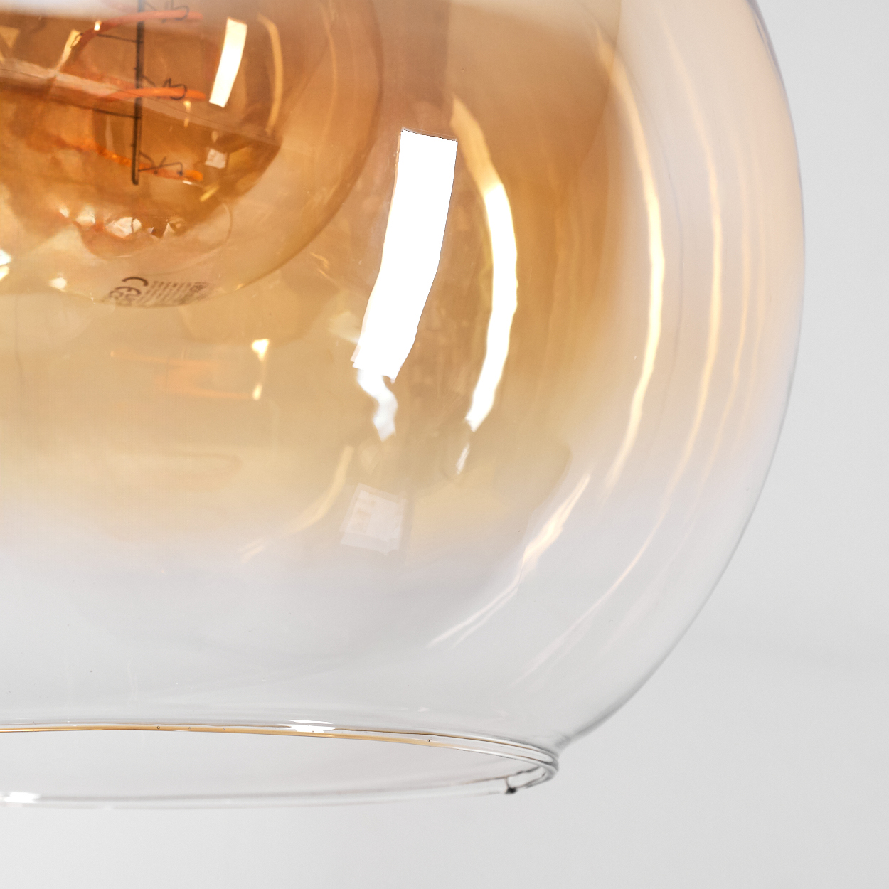 Nahaufnahme einer Glasleuchte. Die Glühbirne befindet sich in einem durchsichtigen Glaskolben. Das Glas hat einen Bernsteinton.