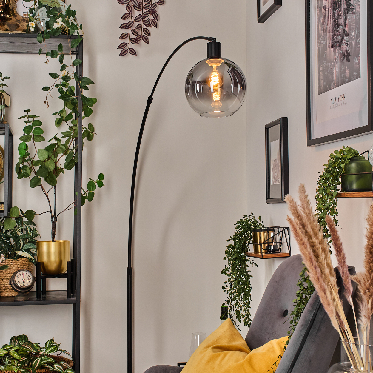 Ein modernes Wohnzimmer mit einer schwarzen Bogenlampe, Pflanzen, einem grauen Sessel und einem New-York-Bild an der Wand.