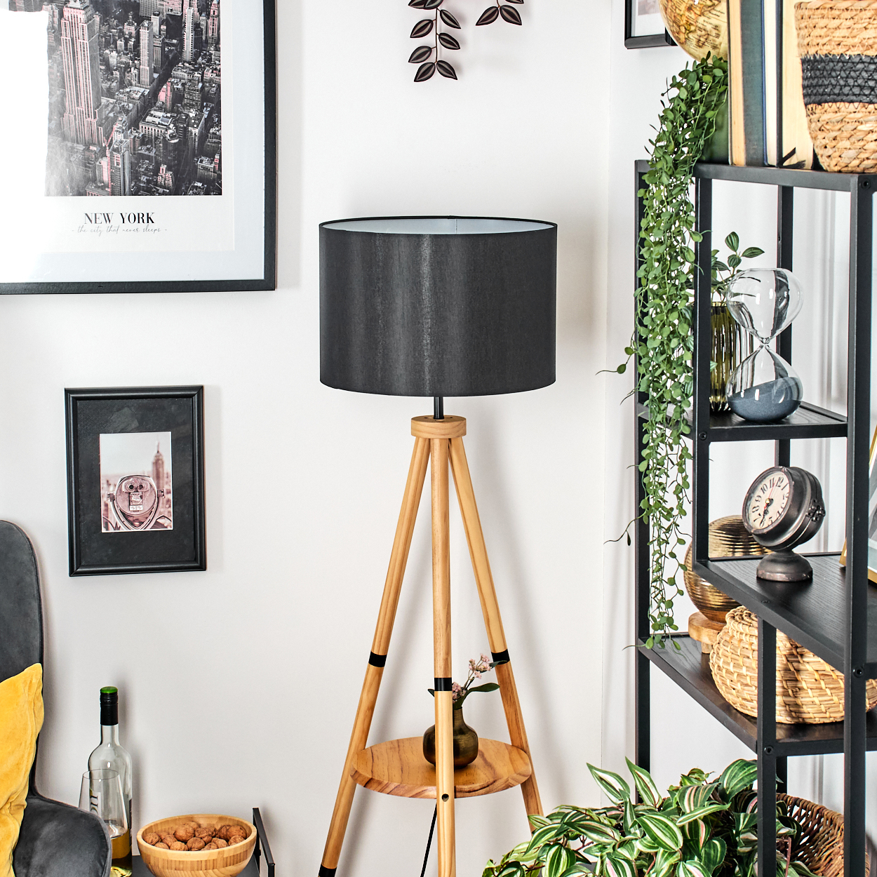 Ein Raum mit einer Holzlampe, einem schwarzen Schirm und einem Bücherregal mit Dekoration. Bilder von New York hängen an der Wand.