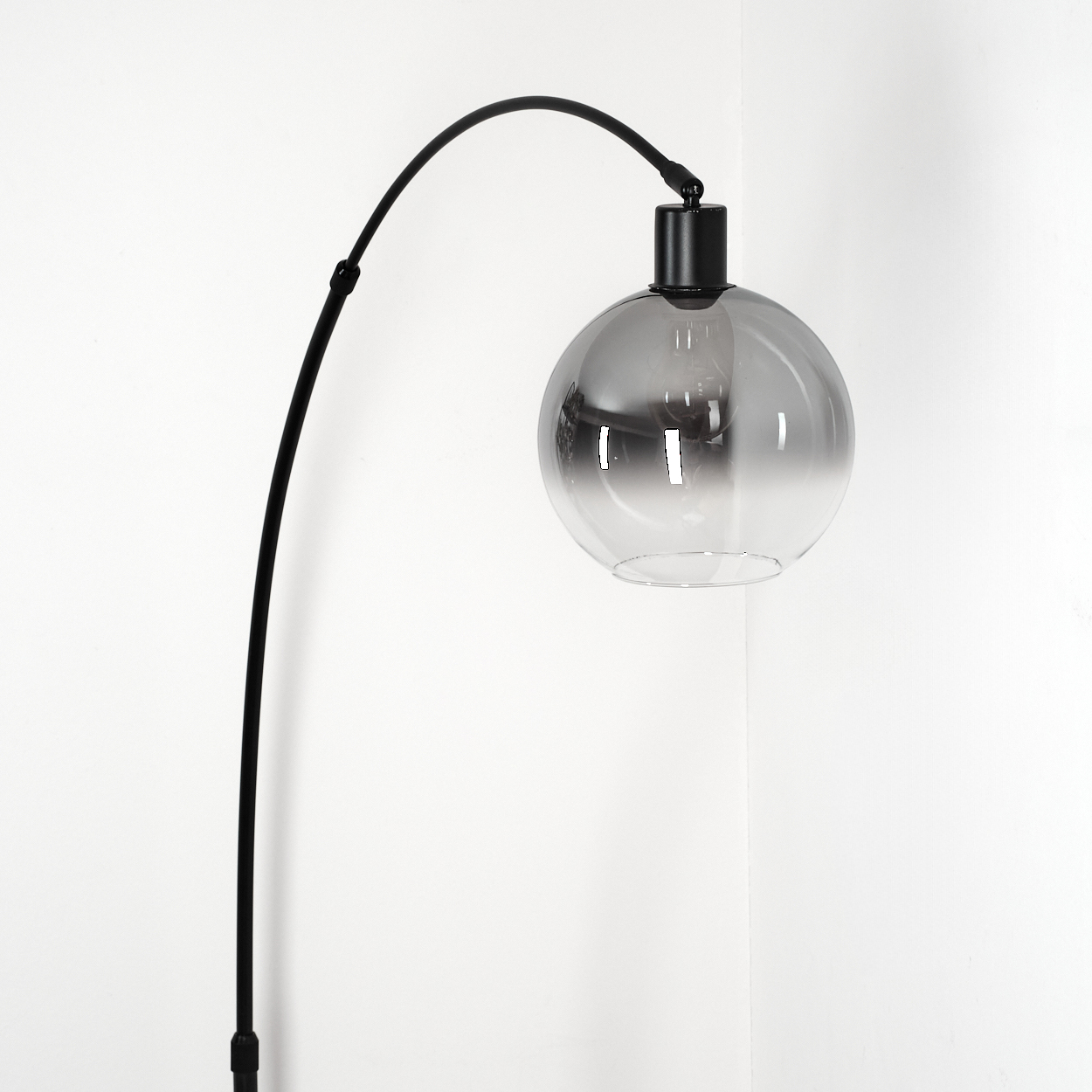 Eine moderne schwarze Stehlampe mit gebogenem Arm trägt einen kugelförmigen, grau getönten Glasschirm. Sie steht vor einer weißen Wand.