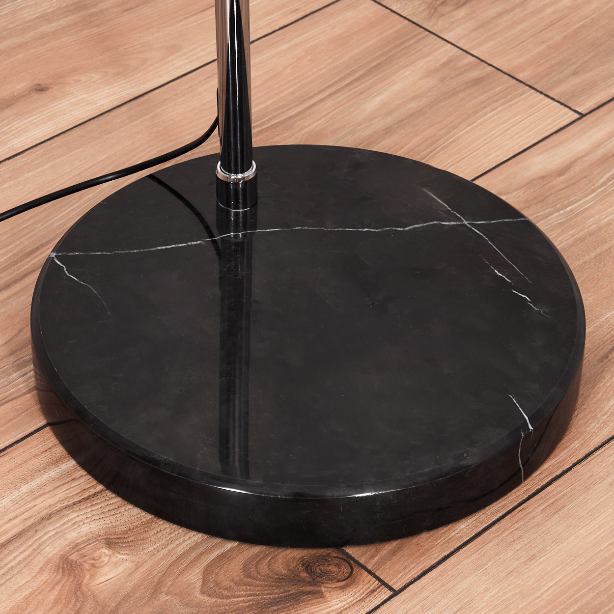Nahaufnahme eines schwarzen Marmor-Lampenfußes. Eine verchromte Lampenstange ragt daraus hervor. Der Boden ist aus Holz.