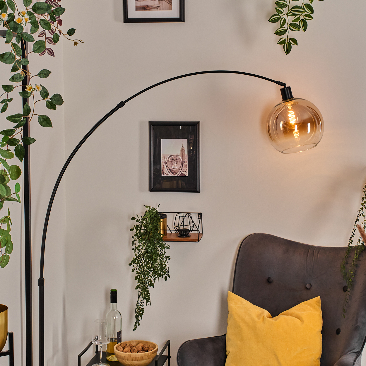 Ein modernes Wohnzimmer mit einer schwarzen Bogenlampe, einem grauen Sessel mit gelbem Kissen und Zierpflanzen.