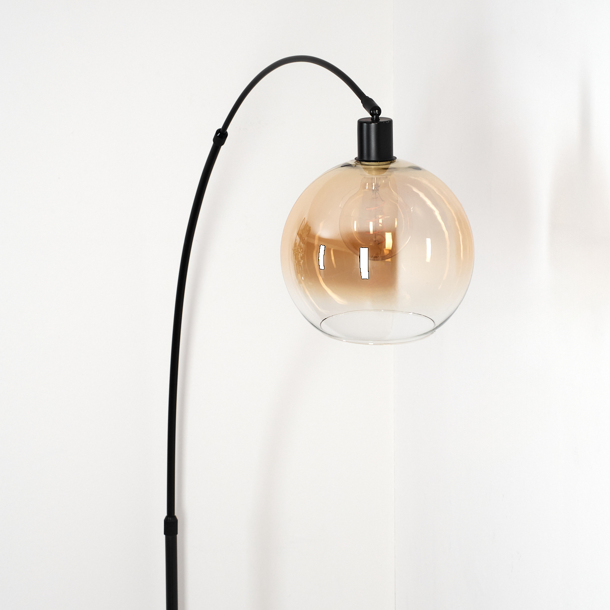 Eine moderne schwarze Stehlampe mit gebogenem Arm trägt einen runden, bernsteinfarbenen Glasschirm. Der Hintergrund ist eine weiße Wand.