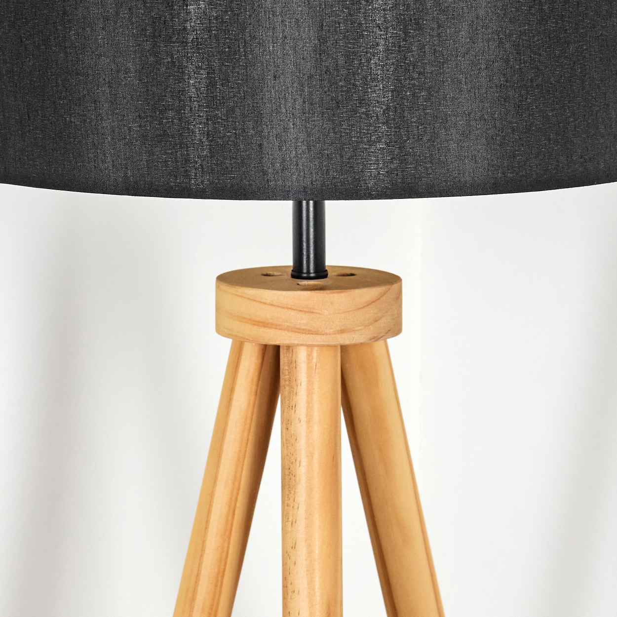 Nahaufnahme einer Lampe. Sie hat einen schwarzen Lampenschirm und ein hölzernes Stativ. Der Hintergrund ist weiß.