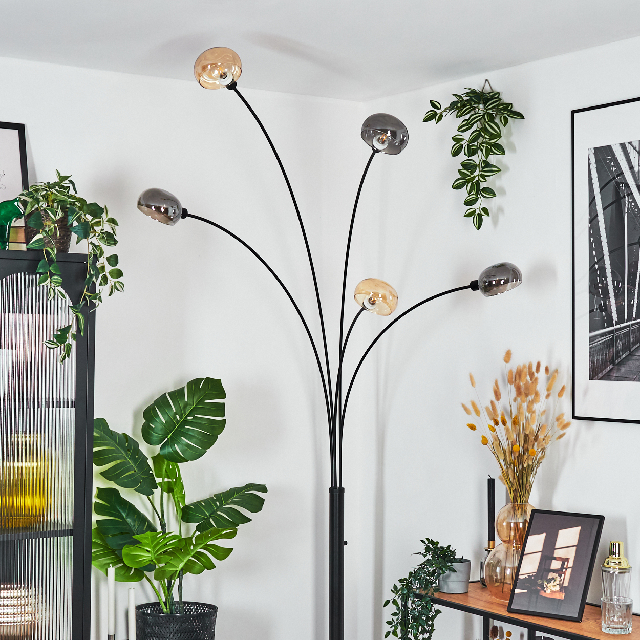 Ein modernes Wohnzimmer mit einer schwarzen Stehlampe mit fünf Kugelleuchten, Pflanzen, einem schwarzen Schrank und gerahmten Bildern.