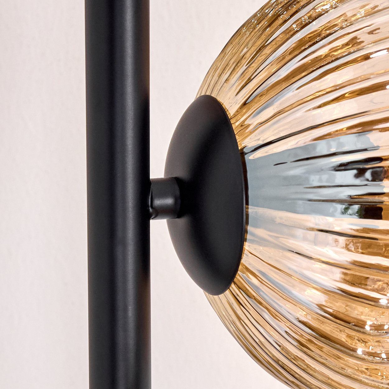 Nahaufnahme einer modernen Lampe. Sie hat einen schwarzen Metallmast und einen kugelförmigen, bernsteinfarbenen Glasschirm mit wellenartigem Design.