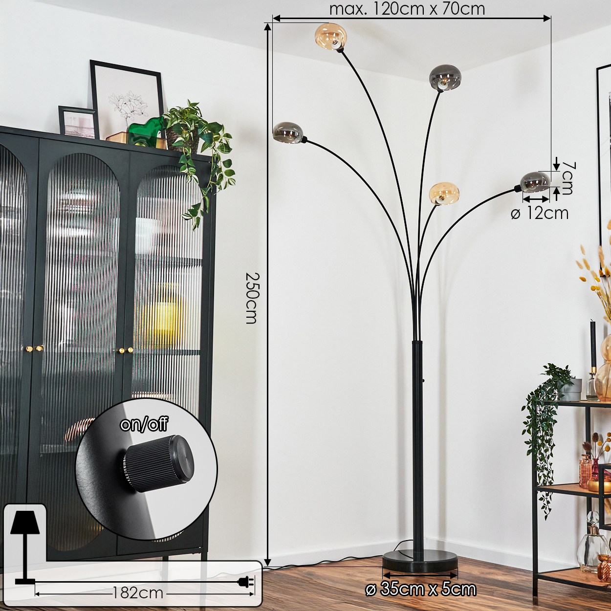 Eine schwarze Stehlampe mit fünf Kugellampen steht in der Nähe eines dunklen Schranks und eines Regals mit Pflanzen. Abmessungen werden angezeigt.
